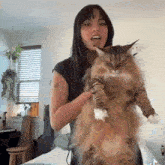 a woman is holding a very large cat in her arms in a living room .