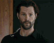 a man with a beard is wearing a black shirt and a security earpiece