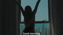 a woman is standing in front of a window with her arms outstretched and the words " good morning " below her