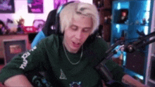 a man with blonde hair is sitting in front of a microphone wearing headphones and a green sweater .