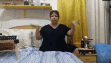 a woman in a black dress is sitting on a bed with her arms outstretched