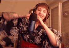 a woman wearing headphones and a blue microphone is smiling