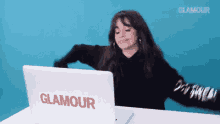 a woman is sitting at a table with her arms outstretched in front of a laptop computer .