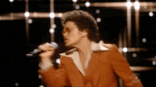 a man in a red suit is singing into a microphone while wearing sunglasses .