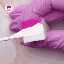 a person wearing pink gloves holds a sponge with pink and white paint on it