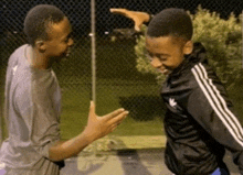 two young men are standing next to each other in front of a chain link fence .