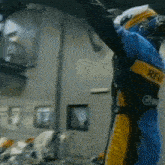 a man in a blue and yellow racing suit is raising his arms in the air