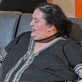 a woman with a choker around her neck sits on a couch .