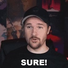 a man with a beard is wearing a hat and a black shirt and says sure !