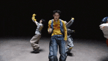 a group of young men are dancing in a dark room and one of them is wearing a yellow shirt with the letter s on it