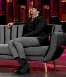 a man in a suit is sitting on a grey couch laughing