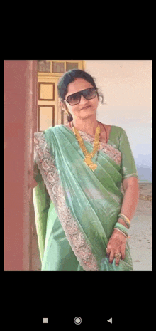 a woman wearing a green saree and sunglasses is standing in front of a door .