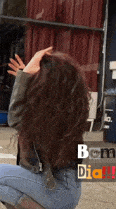 a woman with long curly hair is kneeling down in front of a building with the word dia on the bottom