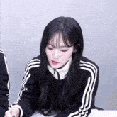 a girl with long black hair wearing a black adidas jacket