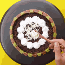 a person is using a wooden spoon to spread whipped cream on top of a chocolate cake
