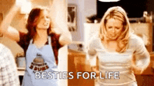 two women are dancing in a kitchen and one of them is wearing an apron .
