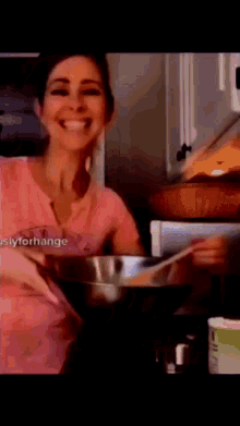 a woman in a pink shirt is smiling while cooking in a kitchen
