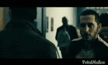 a man with a beard is standing in a dark room with petal malice written on the bottom right