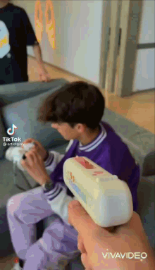 a boy in a purple shirt is sitting on a couch while holding a toy gun .