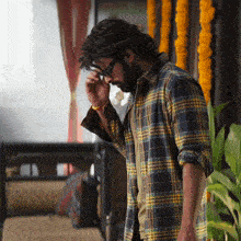 a man wearing glasses and a plaid shirt looks down at something