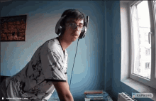 a man wearing headphones and glasses is looking out a window with a kapwng logo in the corner