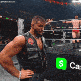 a man in a leather vest stands in a wrestling ring with a $ cash app logo behind him