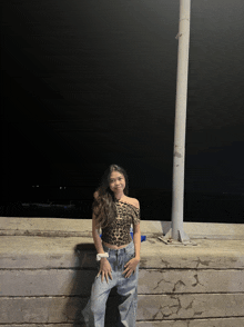 a woman in a leopard print off the shoulder top is standing next to a pole at night