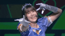 a girl wearing a tiara and gloves is smiling and making a heart shape with her hands