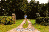 a man is walking down a dirt road with the word hollywood on the side .