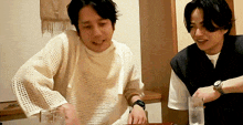 two men are sitting at a table with a glass of water in front of them