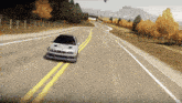 a silver bmw is driving down a road with a mountain in the background