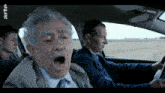a man yawning in a car with arte written on the bottom left