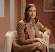 a woman in a brown suit sits in a chair
