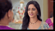 a woman wearing a necklace and earrings talks to another woman .