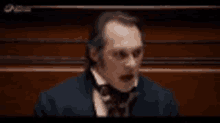 a man in a suit and tie is standing in front of a wooden wall and talking .