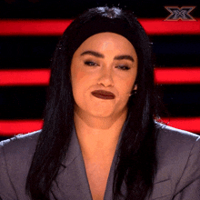 a woman wearing a headband and a blazer is sitting in front of a red and black striped background with an x on it