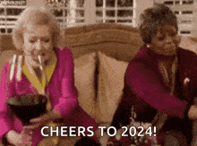 two elderly women are sitting on a couch drinking wine and toasting .