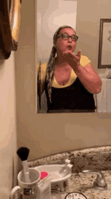 a woman is blowing a kiss in front of a bathroom mirror while wearing glasses .