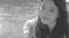 a black and white photo of a woman standing next to a body of water smiling .
