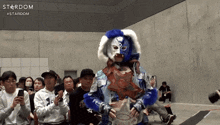 a man in a blue and white mask is holding a trophy in front of a crowd with the word stardom on the bottom right