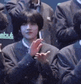a young man in a suit is clapping his hands in front of a crowd .