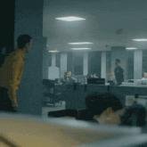 a man in a yellow shirt is standing in front of a computer monitor