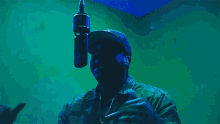 a man wearing a hat stands in front of a microphone in a dark room