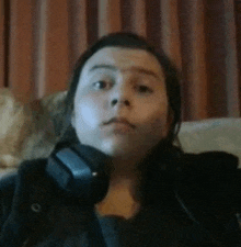 a woman is sitting on a couch wearing headphones and looking at the camera .