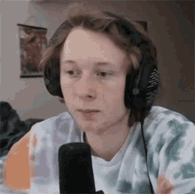 a young man wearing headphones and a tie dye shirt is looking at the camera .