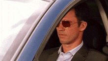 a man in a suit and sunglasses looks out the window of a car