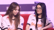two women wearing orange shirts are sitting on a red couch