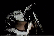 a woman singing into a microphone with a black background