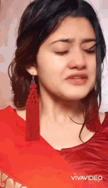 a close up of a woman 's face with her eyes closed wearing red earrings and a red shirt .