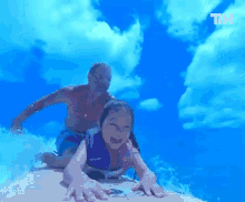 a man and a little girl are riding a wave on a surfboard with the letters th visible in the background